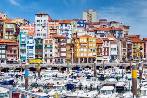 Vibrant townhouses overlook the marina in Bermeo, Spain, against a clear summer sky.