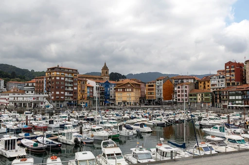 Picturesque harbor in Bermeo, Basque Country, showcasing colorful buildings and boats under a cloudy sky.