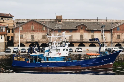 A fishing boat docked at the historic harbor in Getaria, PV, Spain, against a backdrop of old buildings.