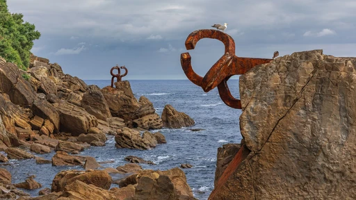 Rust-colored steel arms of Chillida's Peine del Viento reaching from the rocks over the sea at San Sebastián, a gull perched on one.