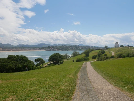 Enjoy the scenic view of Saint-Jean-de-Luz with green pathways, blue skies, and lush greenery along the bay.