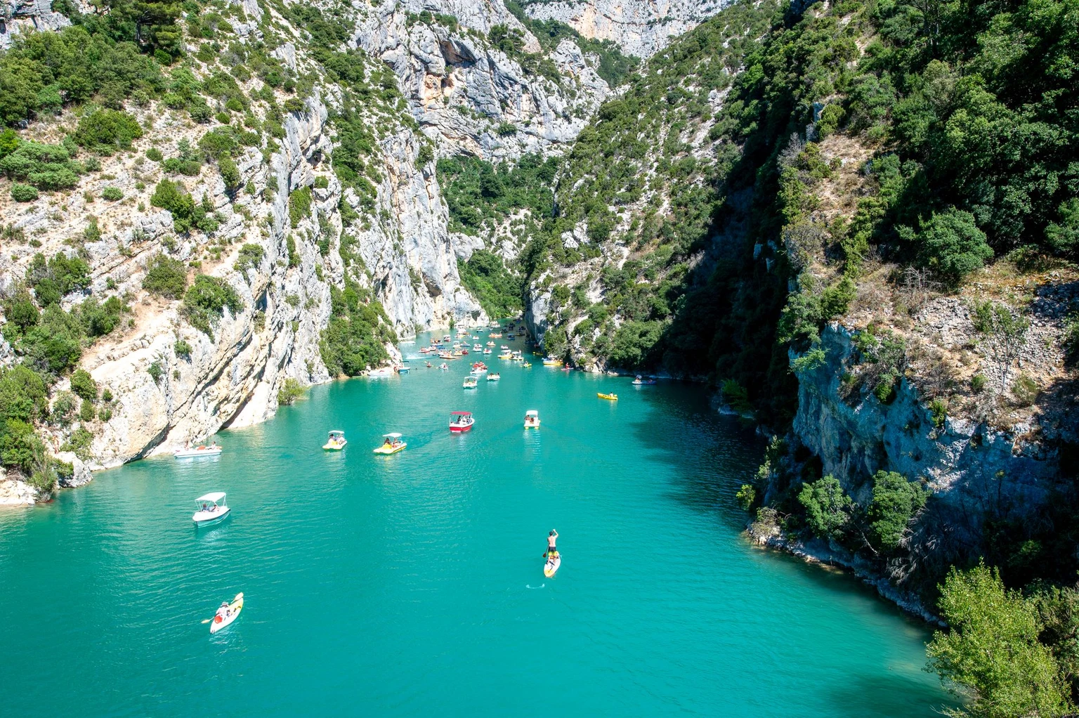 Small boats on the turquoise water at the mouth of the Verdon gorge, seen from above.
