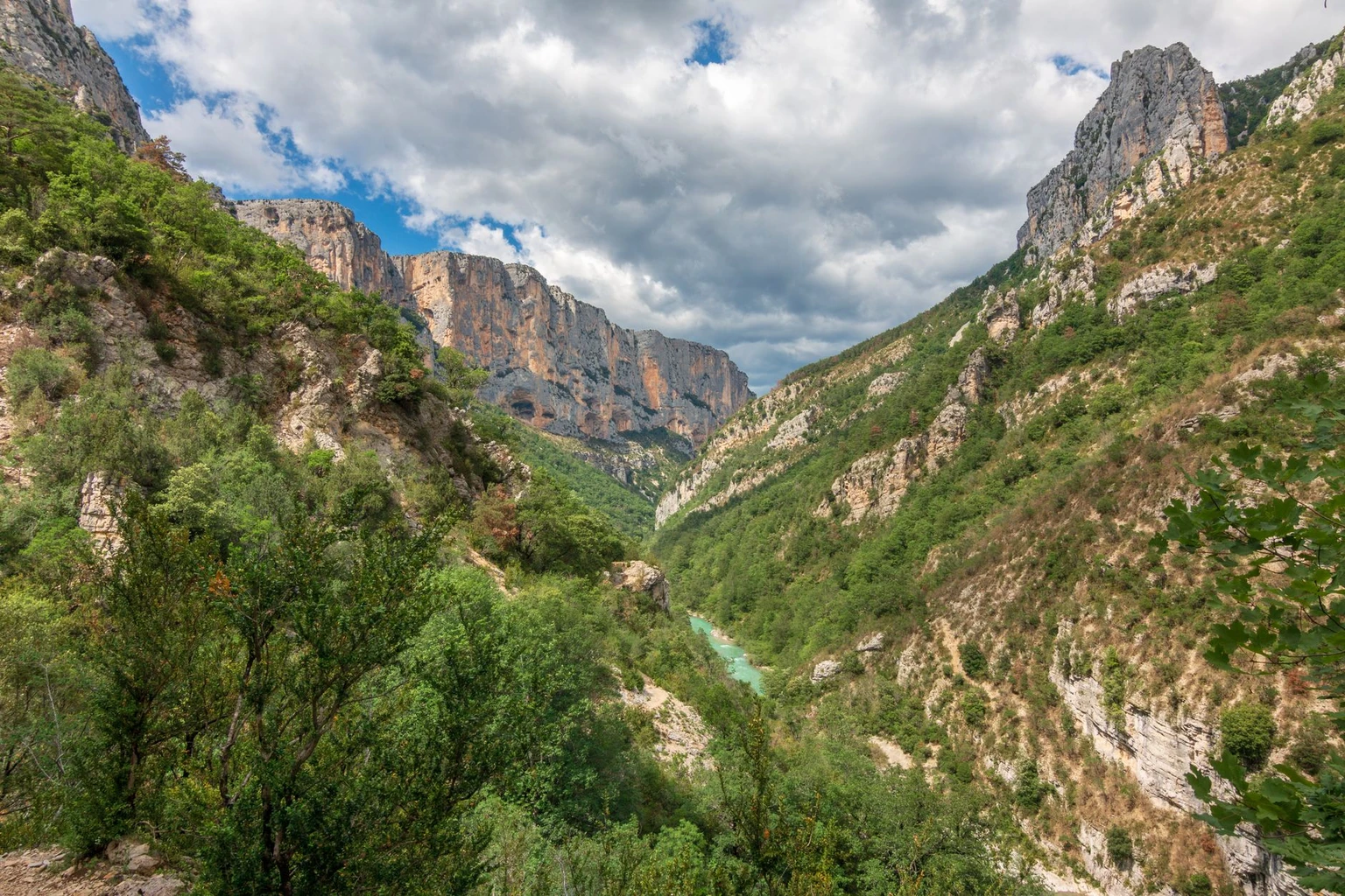 The Verdon gorge winding between green slopes and pale limestone cliffs.