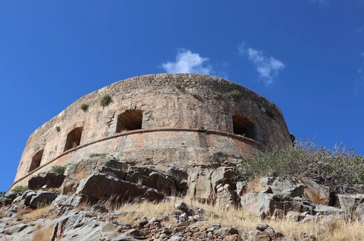 A round stone Venetian bastion on Spinalonga island under a clear blue sky.