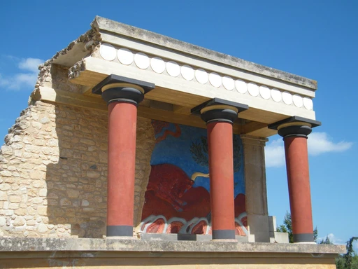 Reconstructed red columns and frescoes at the Knossos palace against a blue sky.