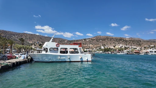 A white tour boat docked in Elounda harbor with the hillside town behind.