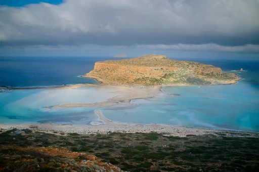 Gramvousa under heavy cloud, seen across the Balos lagoon shallows.