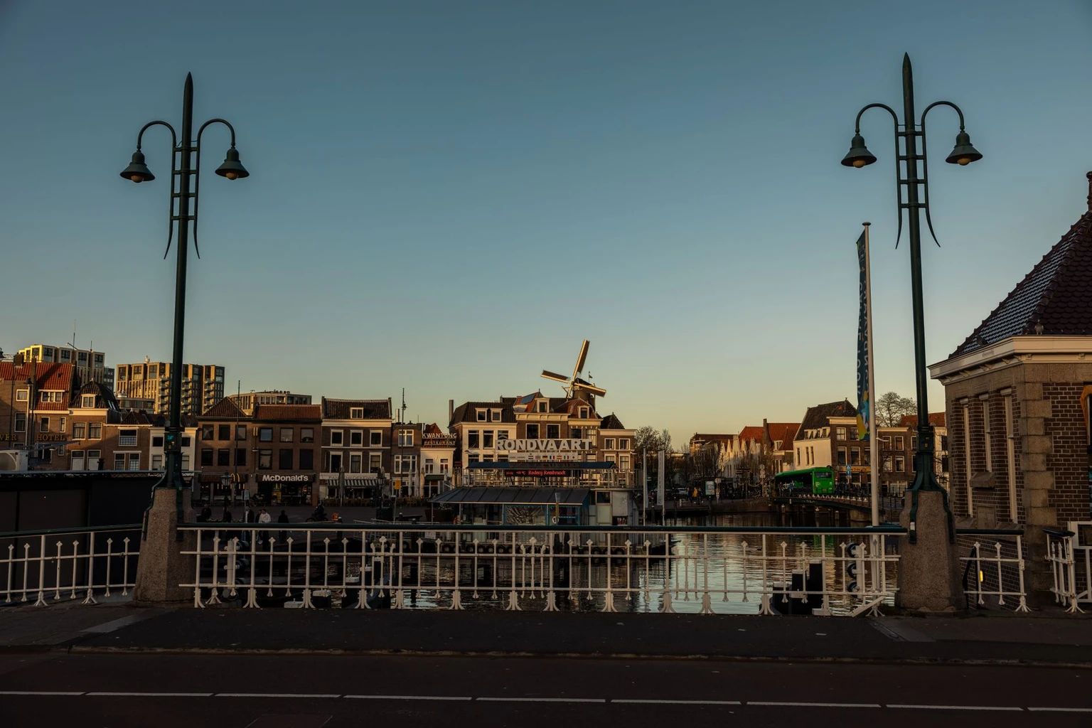 A Leiden canal at twilight with a bridge and a windmill behind the rooftops.