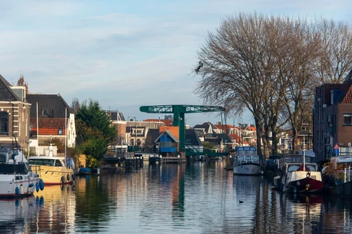 A Leiden canal with moored boats and a bridge reflected in the water.