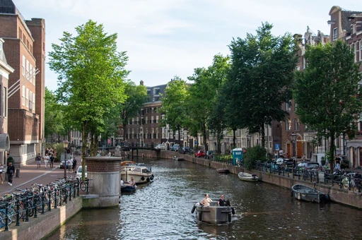 An Amsterdam canal lined with trees and canal houses, with small boats on the water.