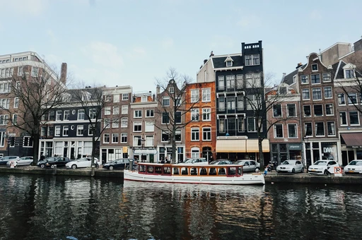 A canal boat on the water in front of a row of Amsterdam canal houses.