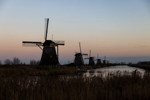 Kinderdijk windmills in silhouette at sunset beside the water.