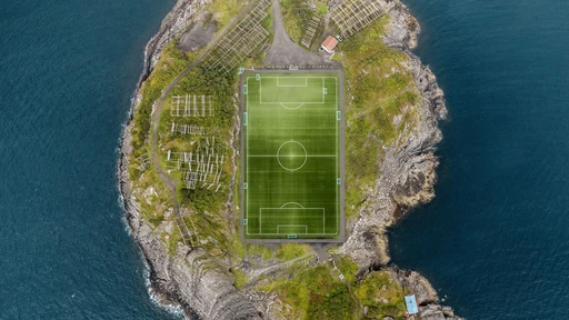 Aerial view straight down on Henningsvær's football pitch, set on a small rocky island with fish-drying racks around it.