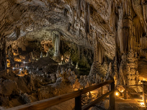 AI-generated illustration: a lit limestone cave with stalactites and a wooden walkway, in the manner of Crete's Dikteon Cave.