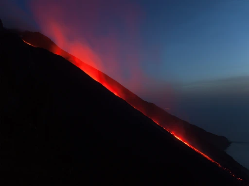 Glowing lava running down the Sciara del Fuoco on Stromboli toward the sea at dusk.