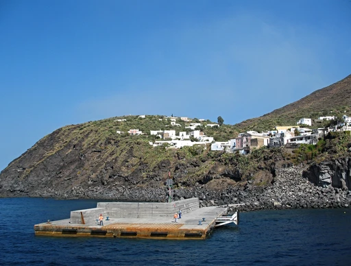 The white houses of Ginostra on the green slope above its small harbor pier, on the far side of Stromboli.
